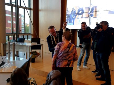 het opspelden van het lintje door burgemeester cees van den bos bij diny jansen. achtergrond de pers met omroep zeeland het opspelden van het lintje door burgemeester cees van den bos bij diny jansen. achtergrond de pers met omroep zeeland